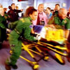 A still from TV show Casualty showing a patient being rushed in on a trolley